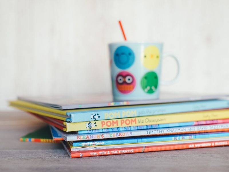 pile of children's books with cup on top