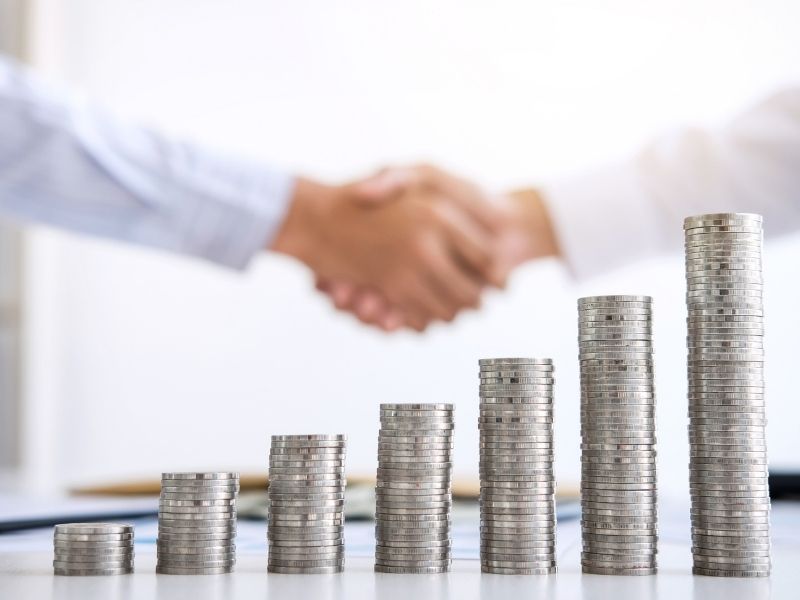 Grant writing image - two hands shaking with piles of coins