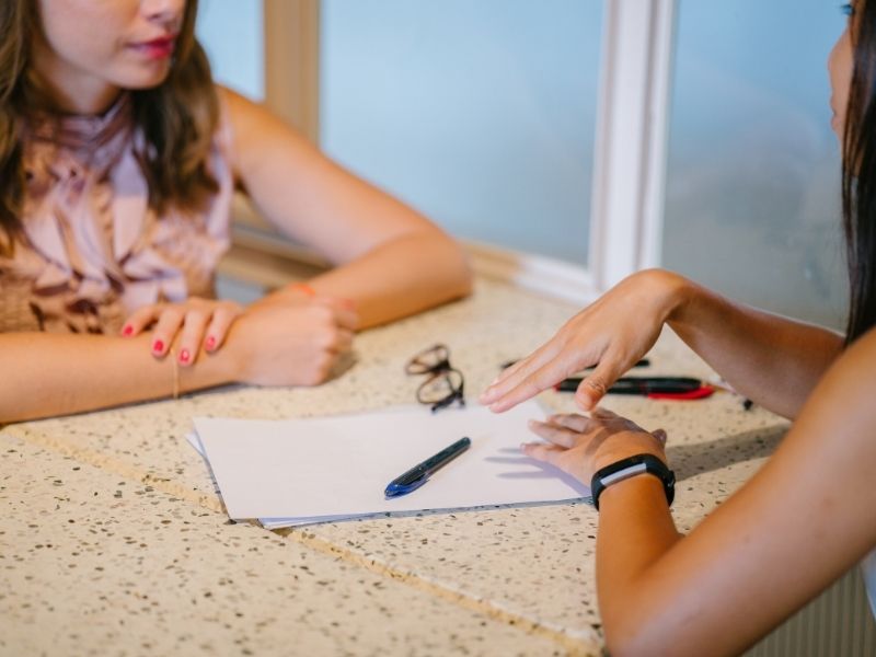 two women talking at table with papers