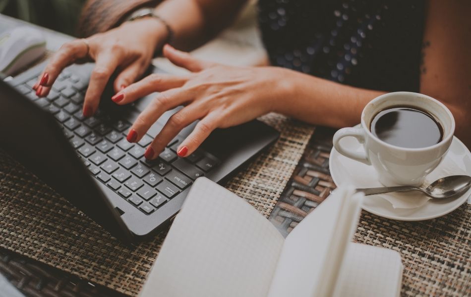 closeup of a woman typing on laptop with coffee on desk